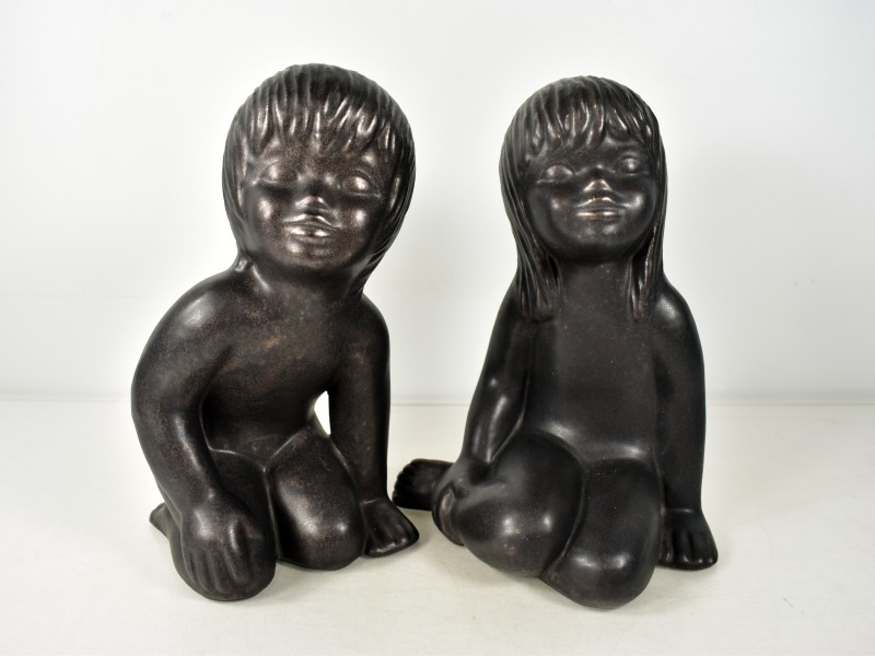 Twee keramische beeldjes van zittende kinderen.